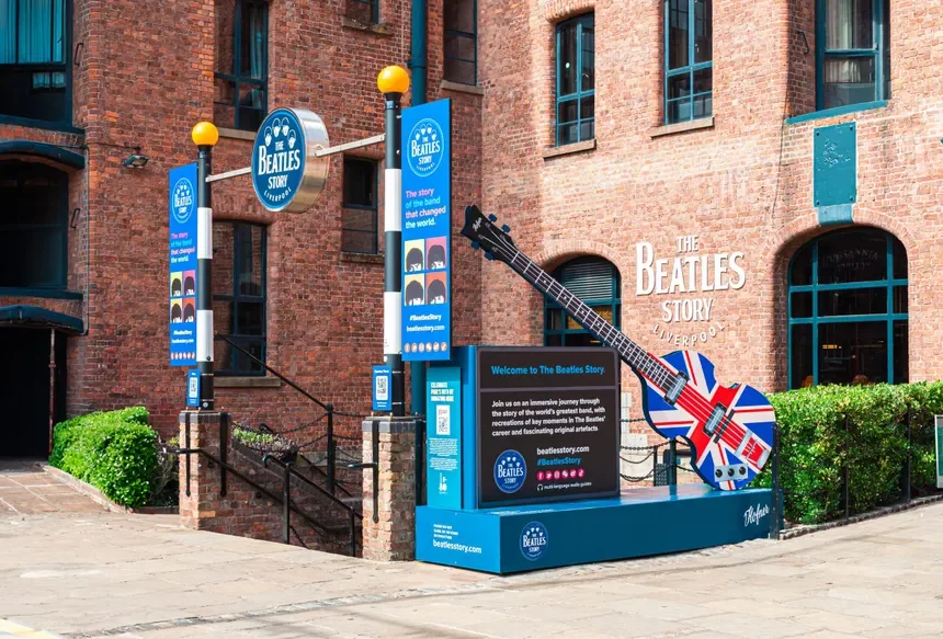Signage and display promoting The Beatles Story museum in Liverpool. Features a guitar with a Union Jack design and information about the museum's offerings.