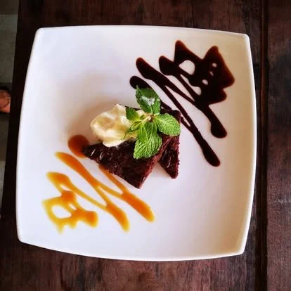 Chocolate dessert with mint leaves, whipped cream, and decorative chocolate and caramel sauce on a white square plate.