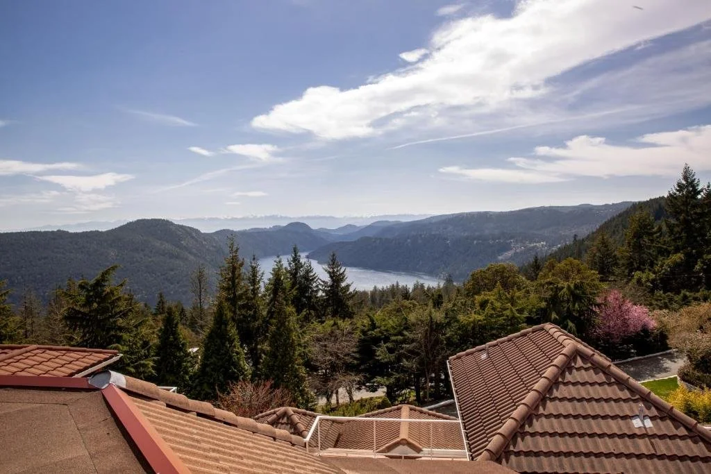 View of rooftops and a landscape with mountains, a river, and a partly cloudy sky in the background.
