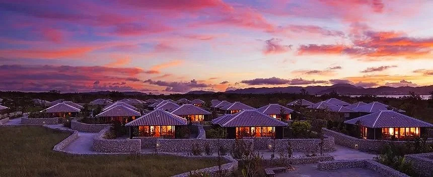 Row of modern cottages illuminated at sunset with a colorful pink and purple sky in the background.