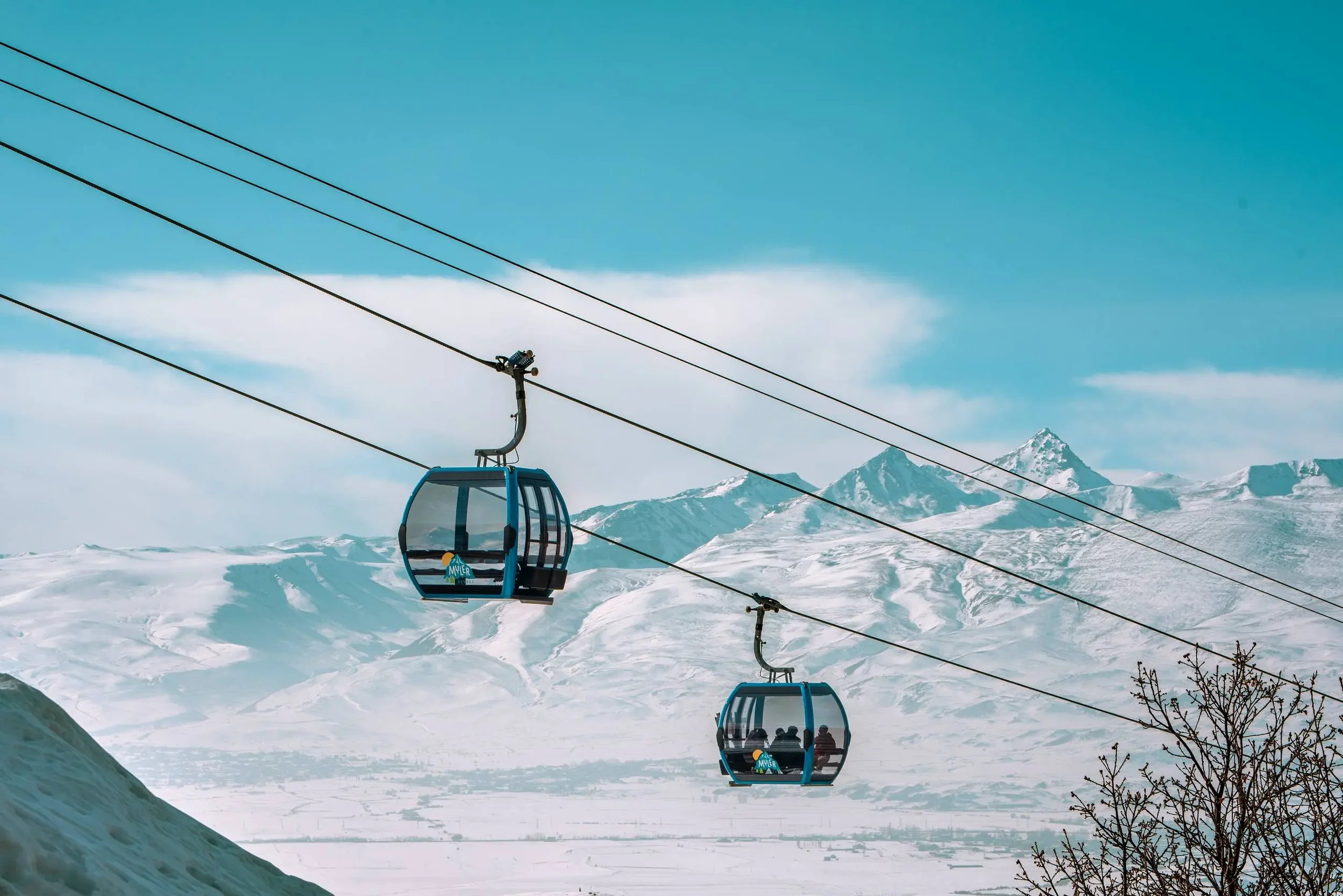 Two blue gondola ski lifts in snowy mountainous landscape with clear blue sky and a few clouds.