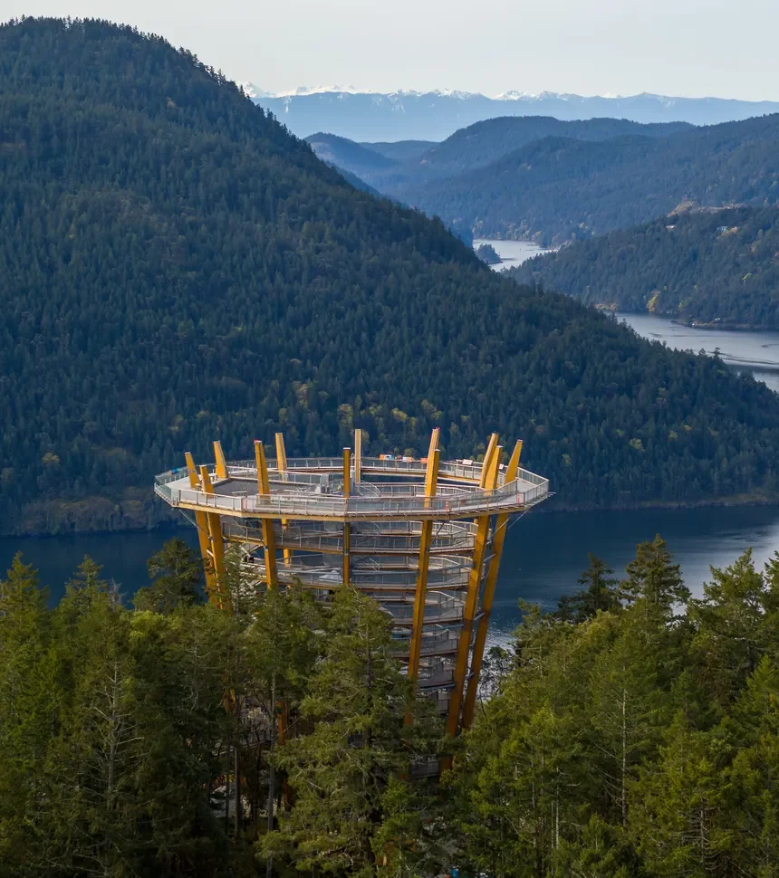A spiral observation tower in a forested mountainous area with a river in the background.