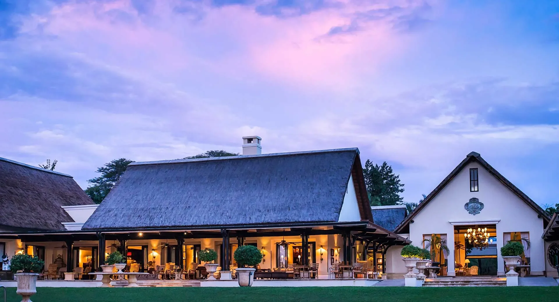 Luxury house with large patio, potted plants, and elegant furniture, under cloudy sky during sunset.