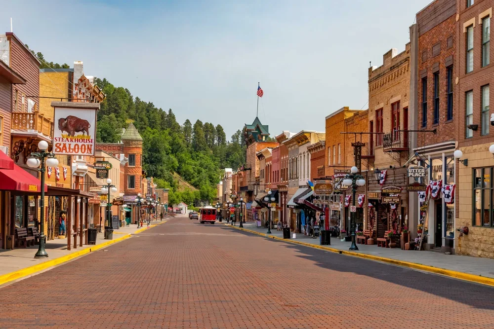 Empty historic Main Street with small shops, restaurants, and lampposts, in a mountain town setting with a hill in the background.
