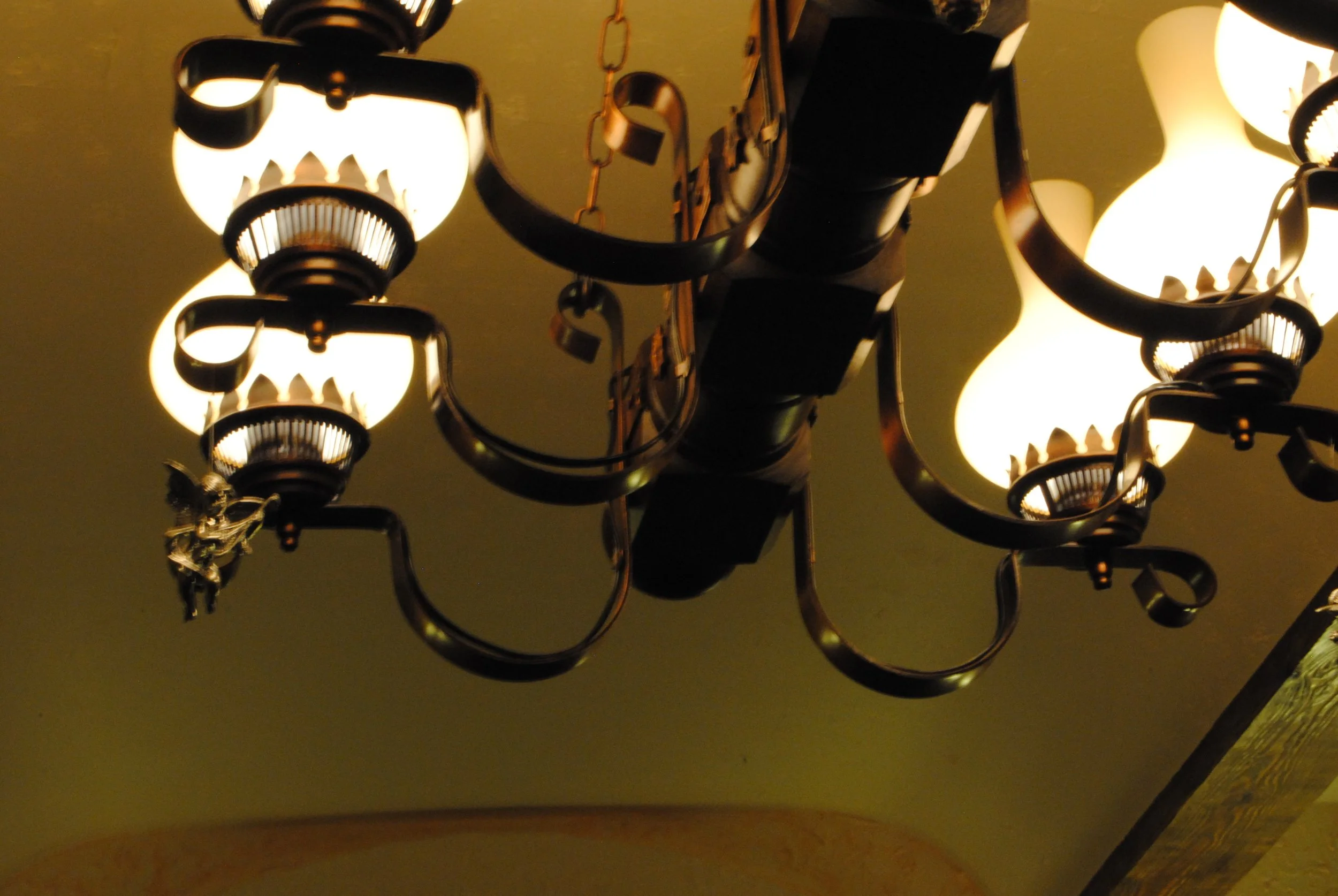 Close-up of a vintage chandelier with several glowing light bulbs hanging from a ceiling.