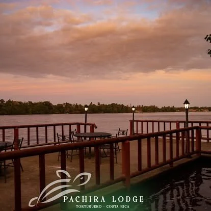 Sunset view over a river with a wooden deck and outdoor chairs at Pachira Lodge in Tortuguero, Costa Rica.