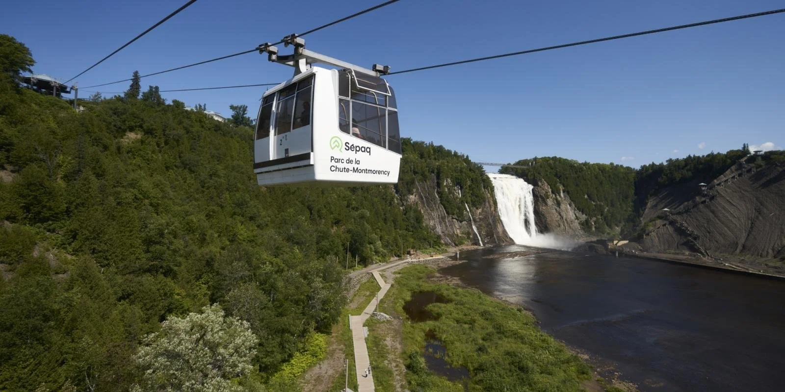 Cable car flying over lush green trees and a waterfall at Parc de la Chute-Montmorency in Quebec.