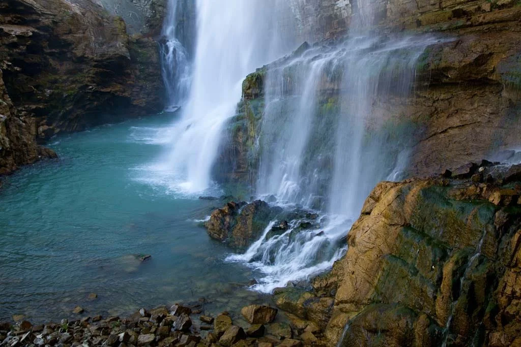 A scenic waterfall cascading into a river surrounded by rocky cliffs.