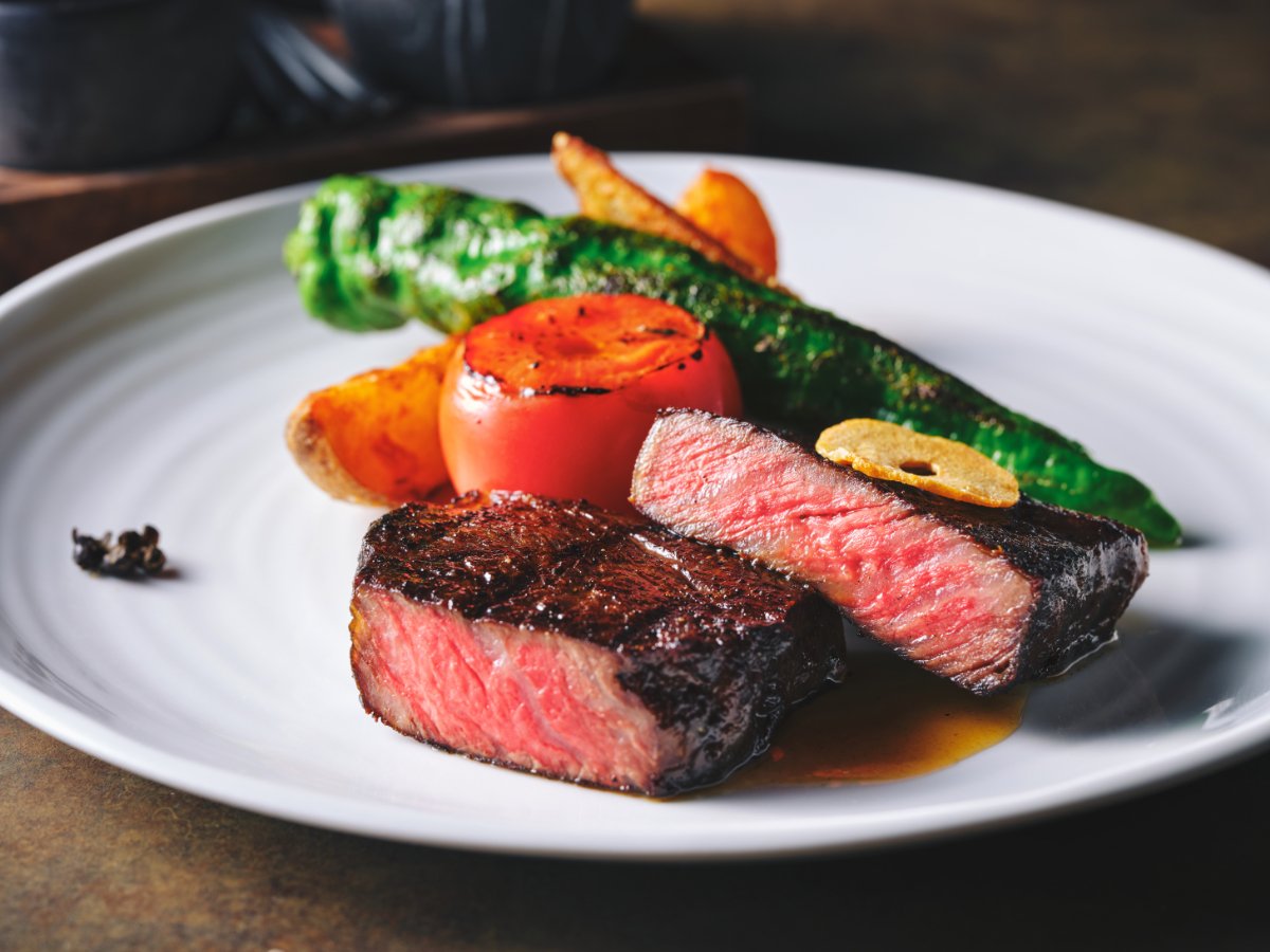 Cooked steak with grilled vegetables on a white plate.