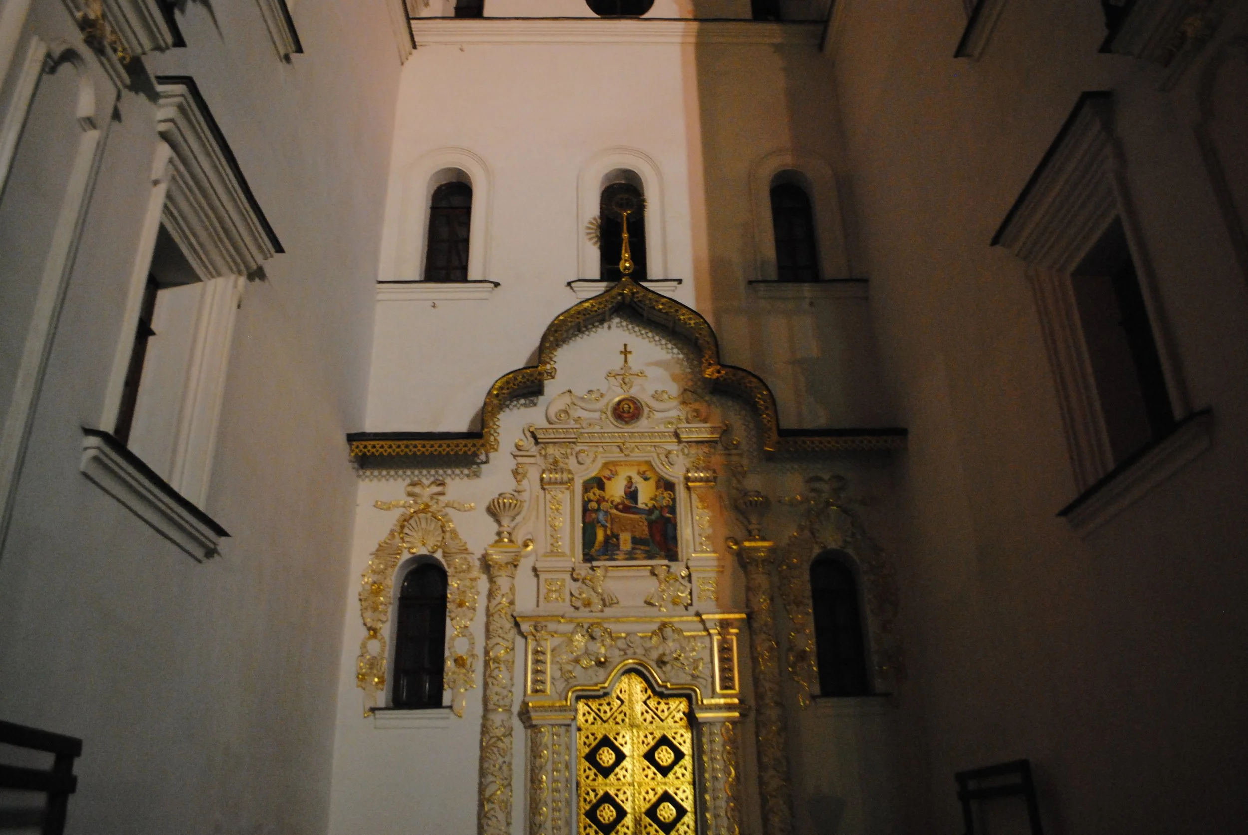 Interior view of a church with ornate gold and white altar, religious paintings, and decorative architectural elements.