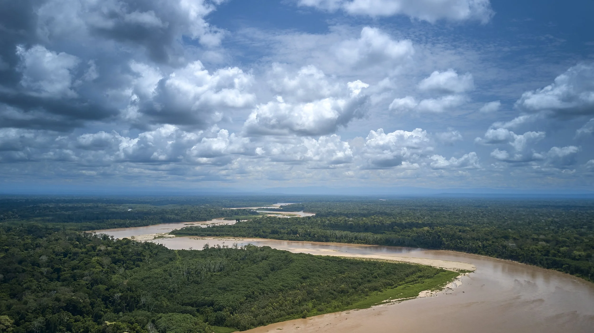 Aerial view of a river winding through a dense green forest under a cloudy sky.