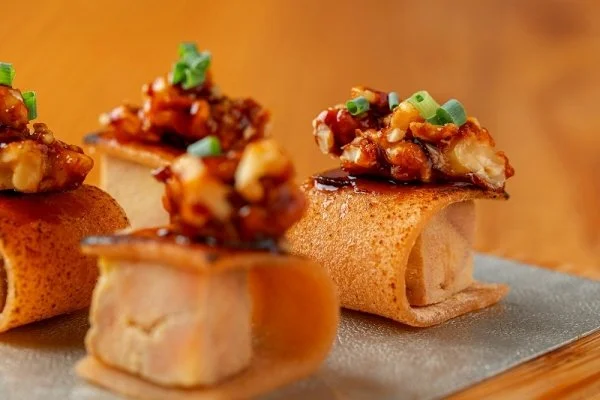 Close-up of mini Asian-inspired appetizers with crispy shell, topped with a spicy mixture of chopped green onions and sauce, served on a gray slate plate.