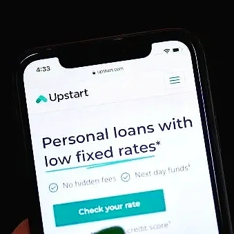 A cute Australian Shepherd dog with a blue merle coat, wearing an orange bandana, lying in a cozy dog bed near a window.