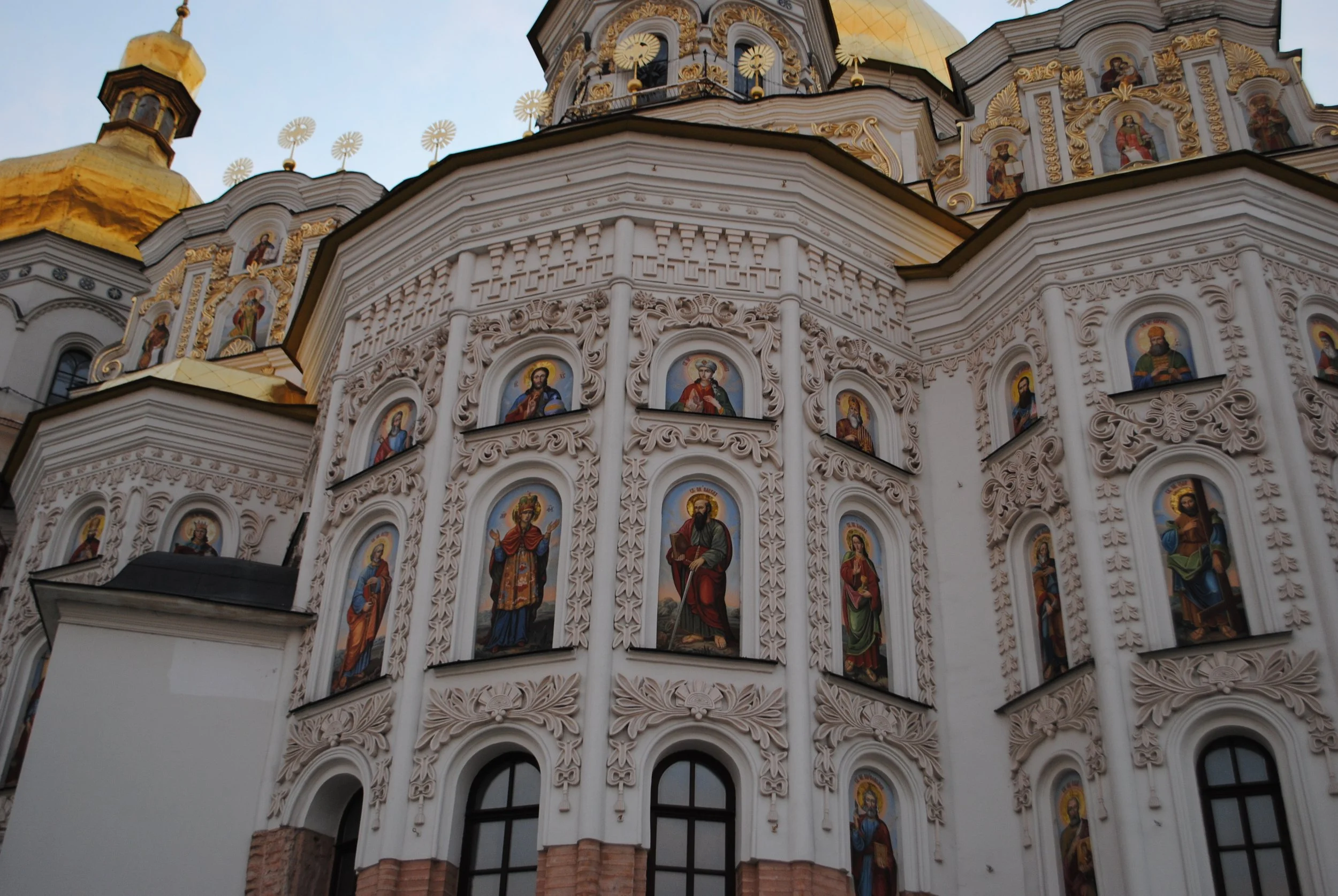 Close-up of a richly decorated Orthodox church with colorful religious icon paintings on white ornate facades and gold domes at sunset