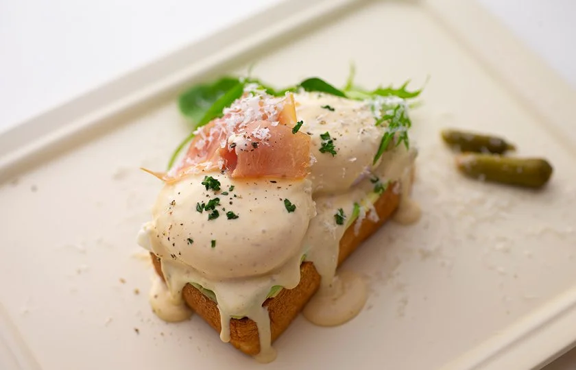 Poached eggs topped with ham, herbs, and cheese served on toast with green beans on the side.