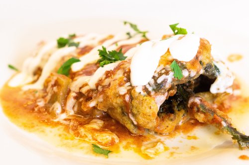 Close-up of fried eggplant with tomato sauce, sour cream, and cilantro on a white plate.