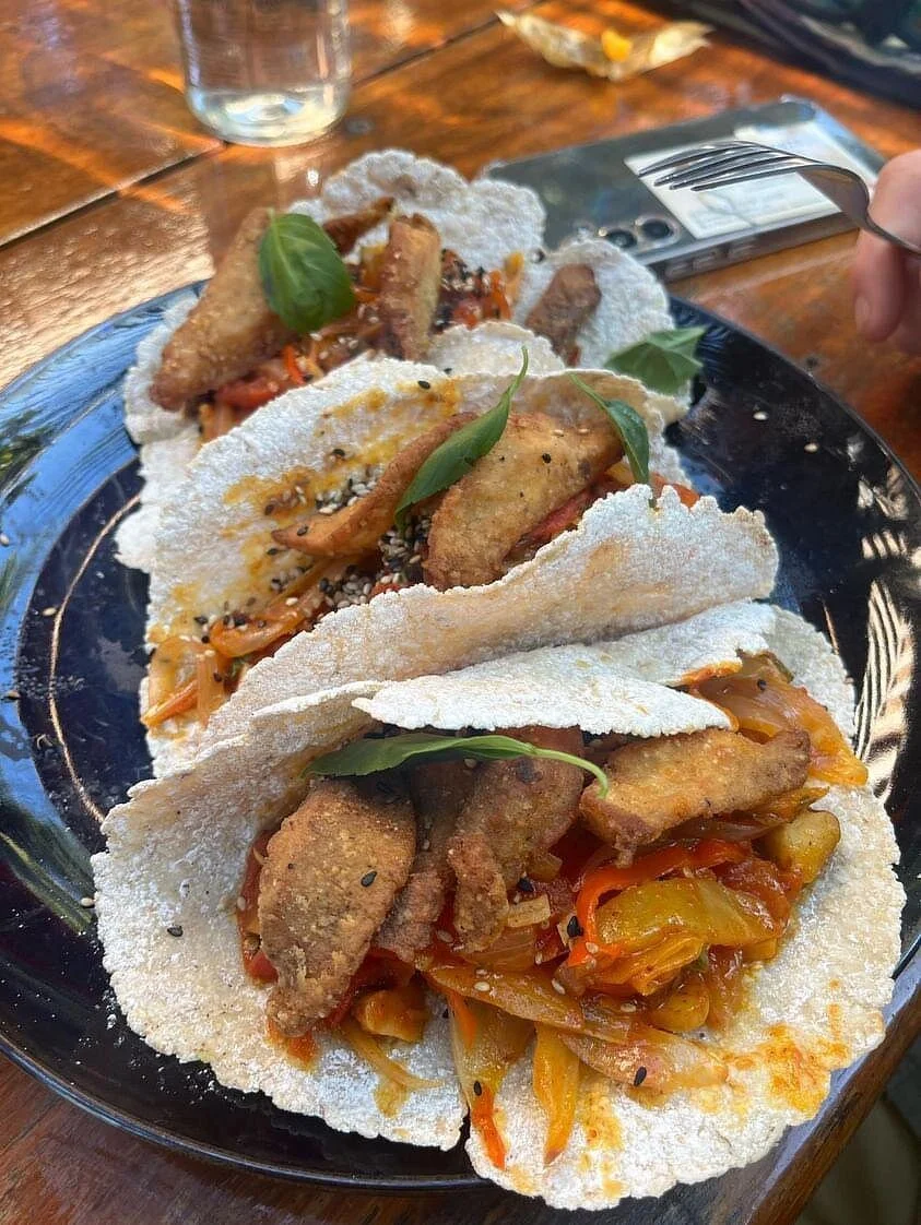 Three fish tacos with fried fish, shredded vegetables, and garnished with basil leaves on a black plate.