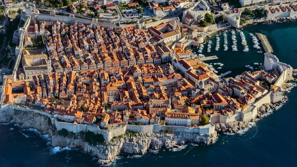 Aerial view of a historic coastal city with tightly packed buildings and red-tiled roofs surrounded by fortified walls and a marina with boats on the water. Kiev November 2011, Marina Parrish ©