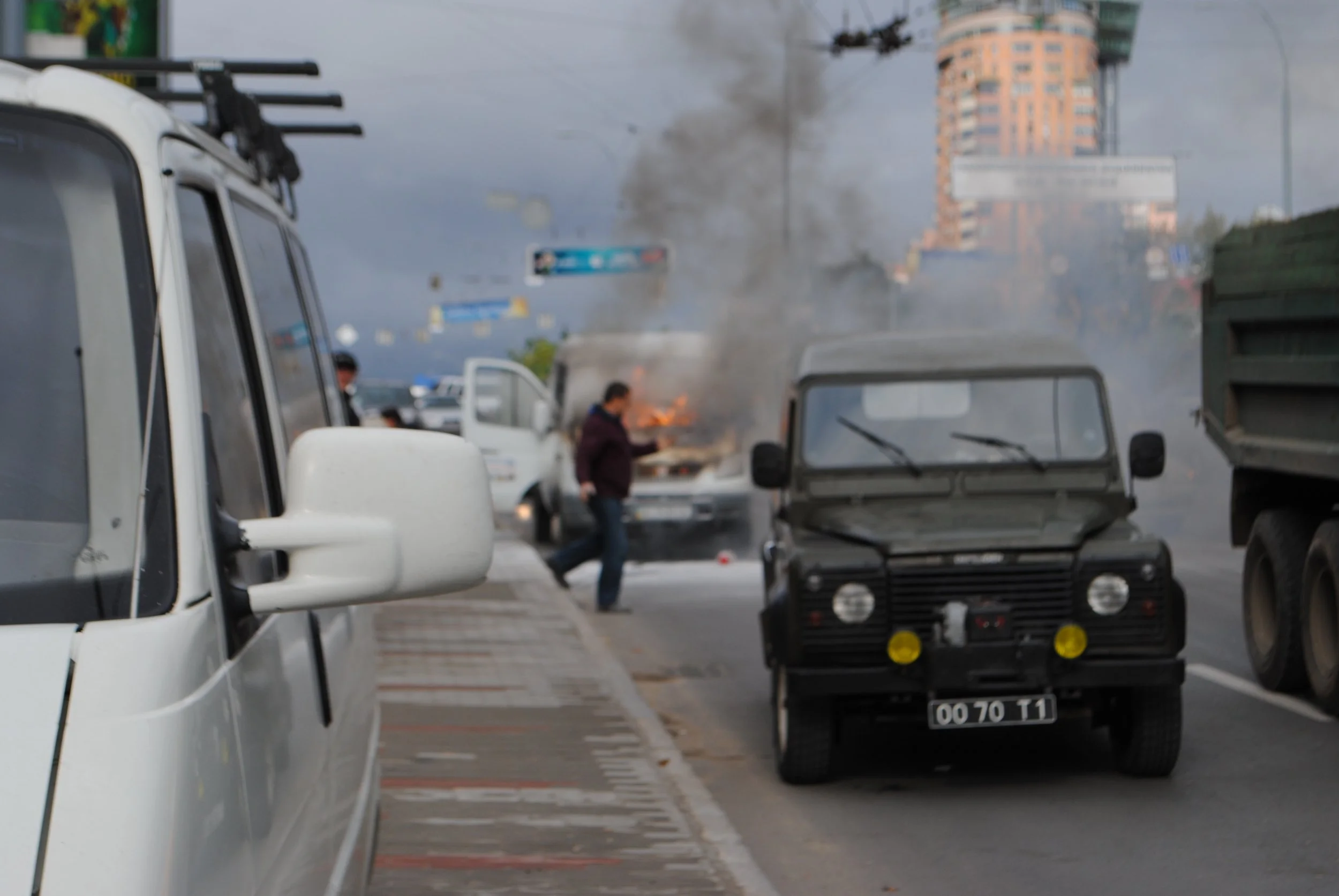 A street scene with vehicles, smoke rising from a fire, and people walking nearby during the daytime. Kiev November 2011, Marina Parrish ©