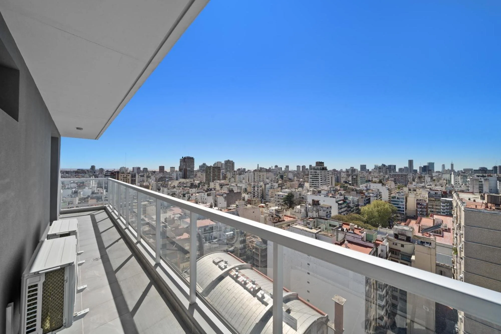 Balcony view overlooking a city with many high-rise buildings under a clear blue sky.