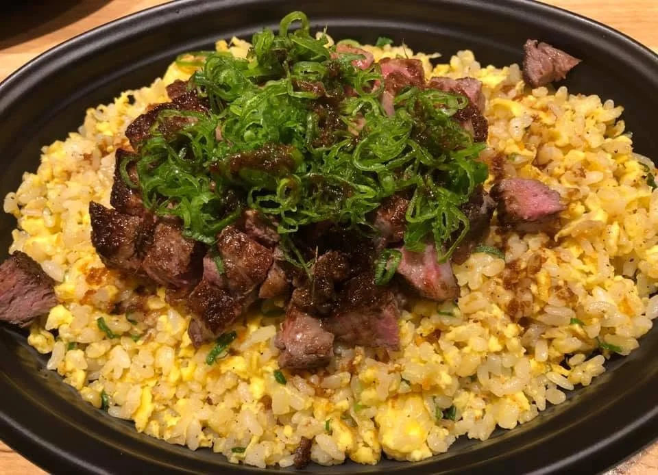 Fried rice topped with diced beef and chopped green onions in a black bowl.