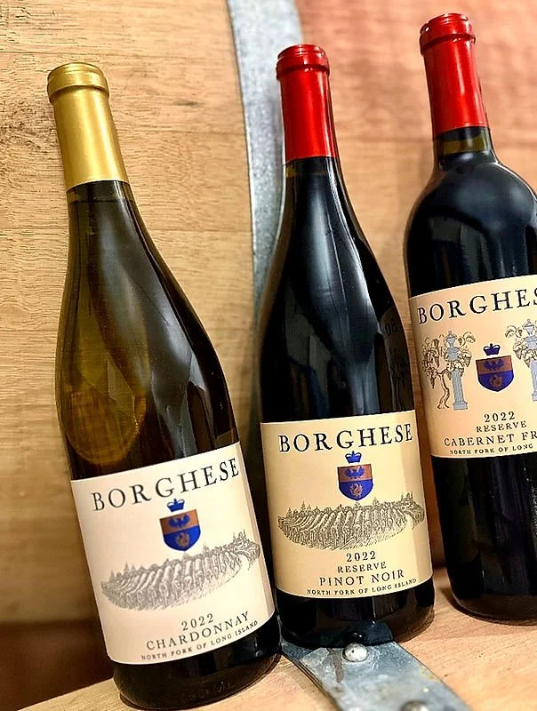 Three bottles of Borghese wine on a wooden surface, with two bottles of Reserve Pinot Noir and one bottle of Chardonnay from 2022.
