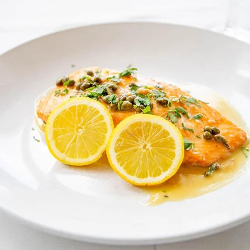 Salmon fillet garnished with chopped herbs, capers, and lemon slices on a white plate