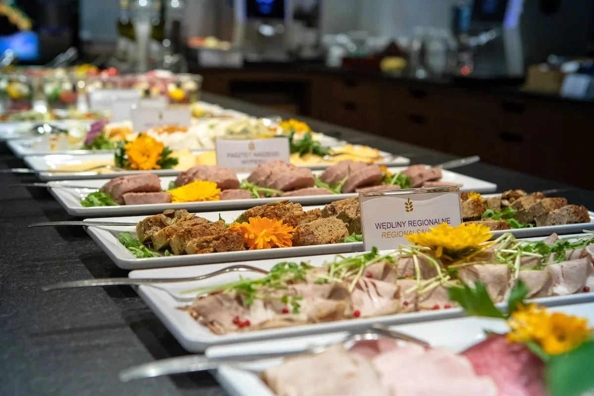 A buffet of assorted regional meats and salads decorated with yellow and orange flowers.