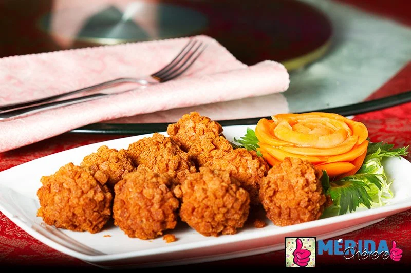 Fried chicken balls served with a decorative carrot flower and green garnish on a white plate.