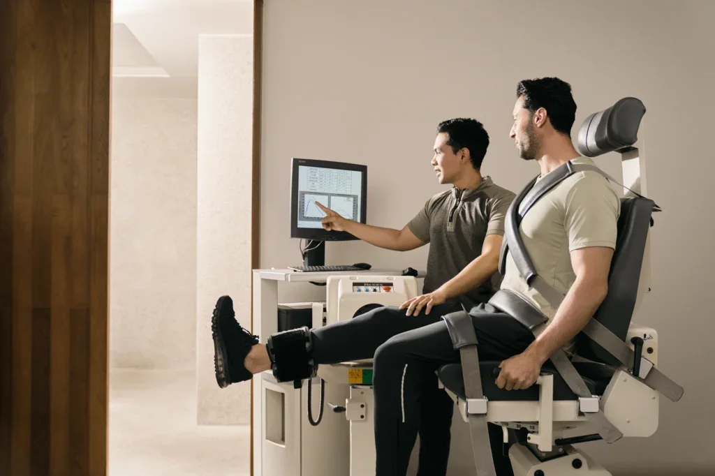 A man in a medical chair connected to a harness being tested by a technician at a hospital.