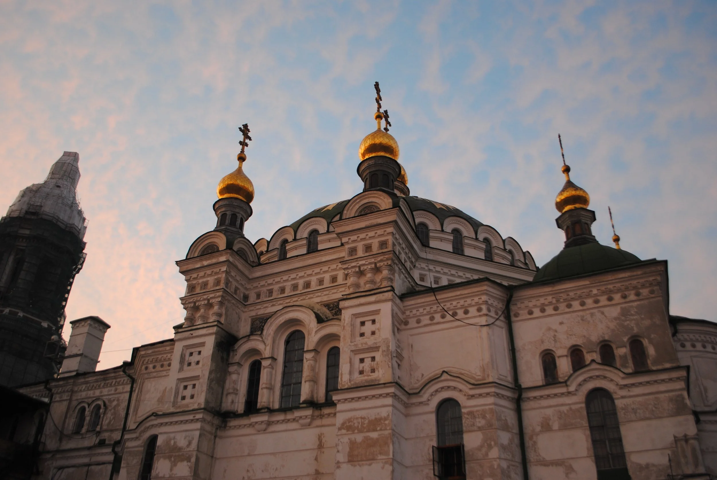A church with golden onion domes and cross finials under a evening sky with scattered clouds.