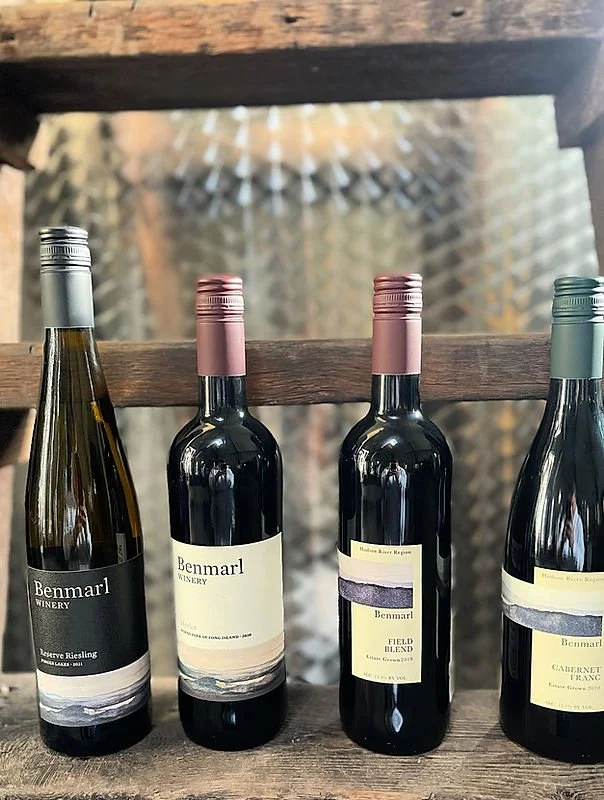 Four bottles of wine from Benmarl Winery, with various labels and pink or metallic screw caps, displayed on a rustic wooden surface.