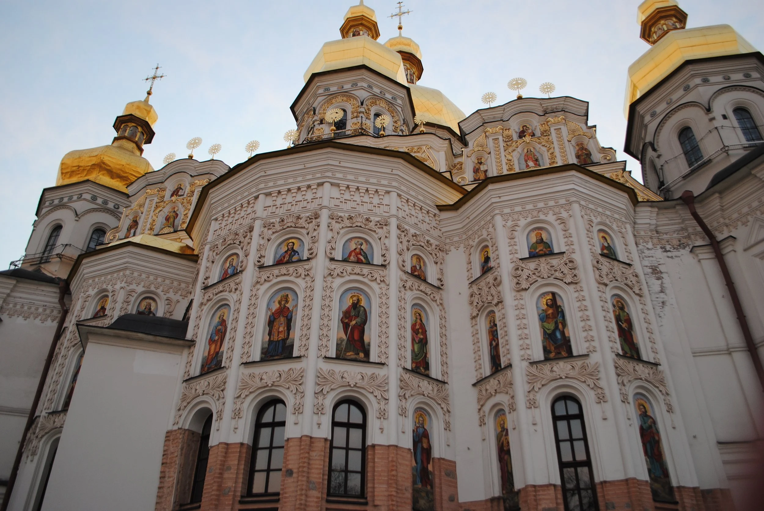 A church with golden domes and ornate exterior decorations, including religious icons, set against a clear sky.