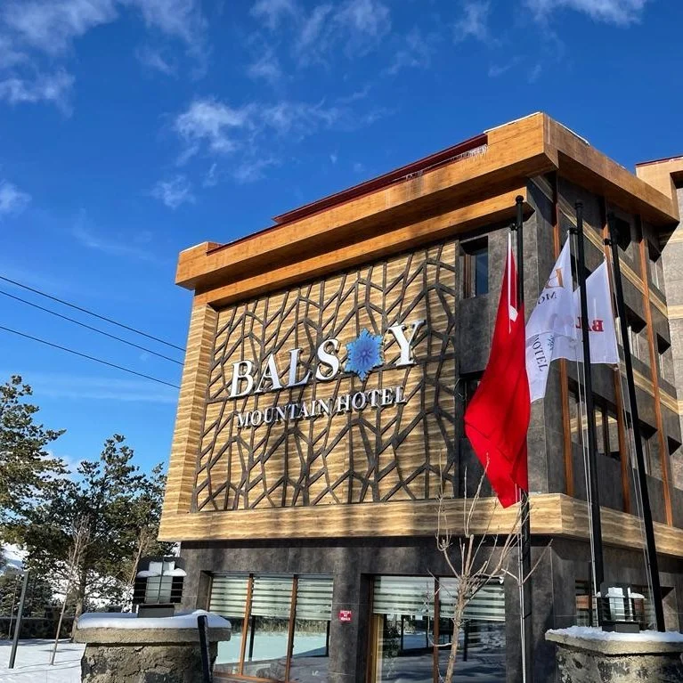 Exterior of Balsy Mountain Hotel with flags and a geometric decorative facade, under a clear blue sky.