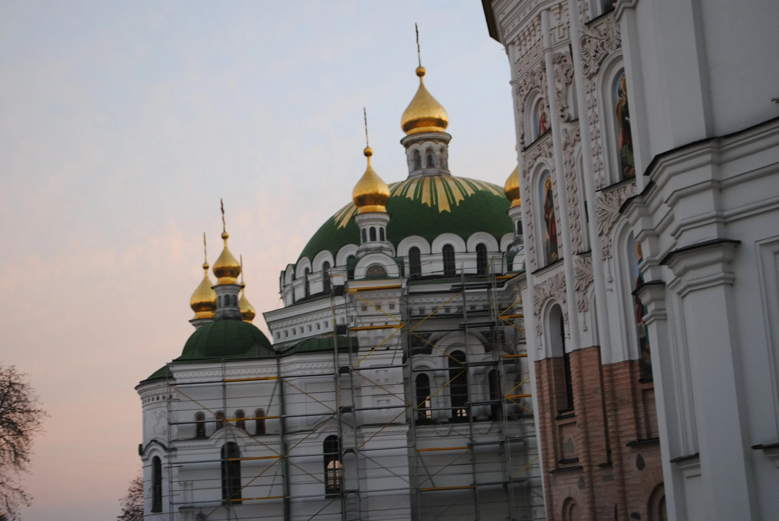 A church with golden domes and white ornate walls, with some construction scaffolding visible on the building.
