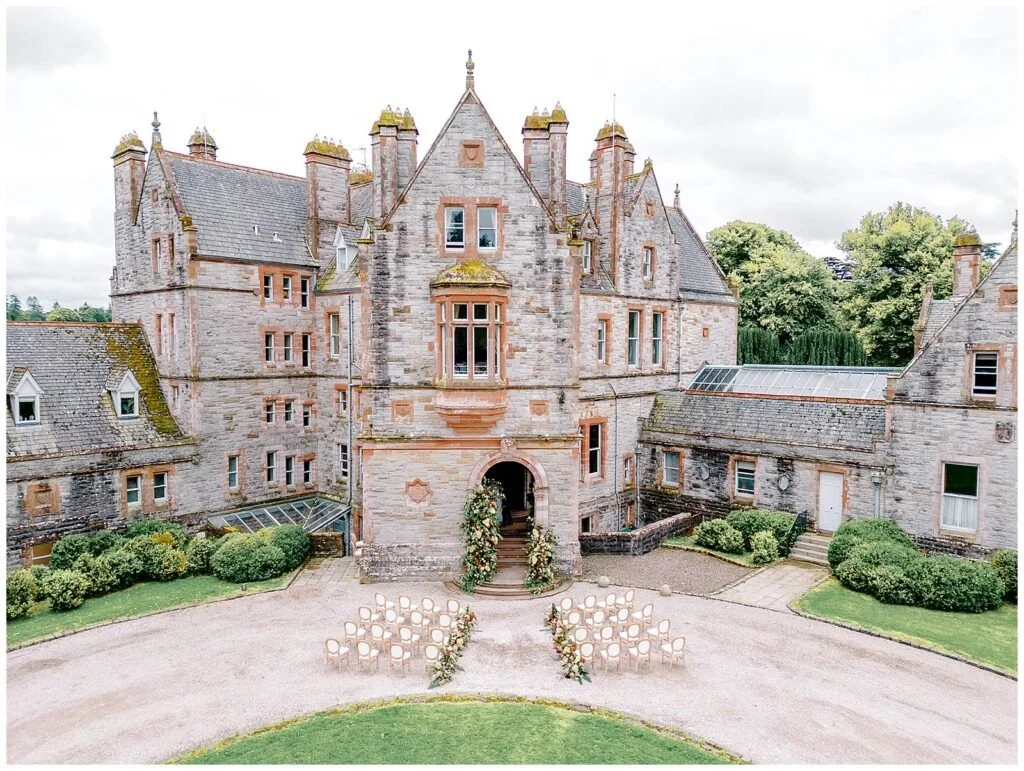 A historic stone castle set up for an outdoor wedding ceremony with chairs and floral decorations in front.