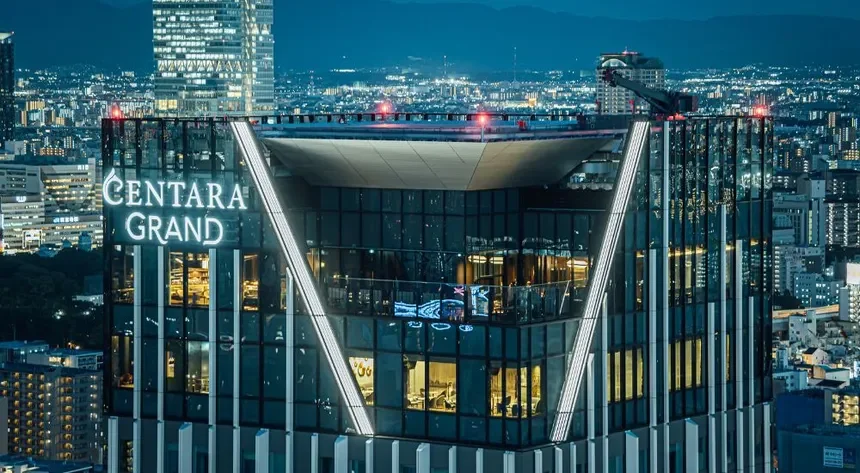 Nighttime cityscape with a modern glass hotel building labeled 'Centara Grand' illuminated in the foreground.