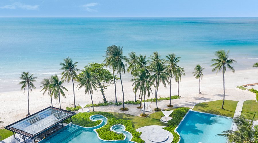 Beautiful tropical beach with white sand, turquoise ocean, palm trees, and a luxurious pool area.