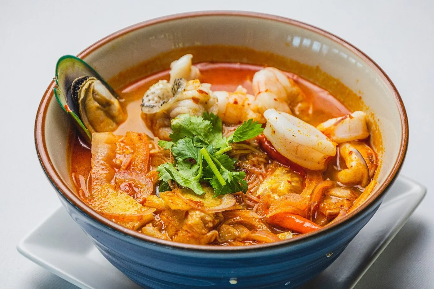 A bowl of seafood noodle soup with shrimp, squid, mussels, and cilantro garnished on top.