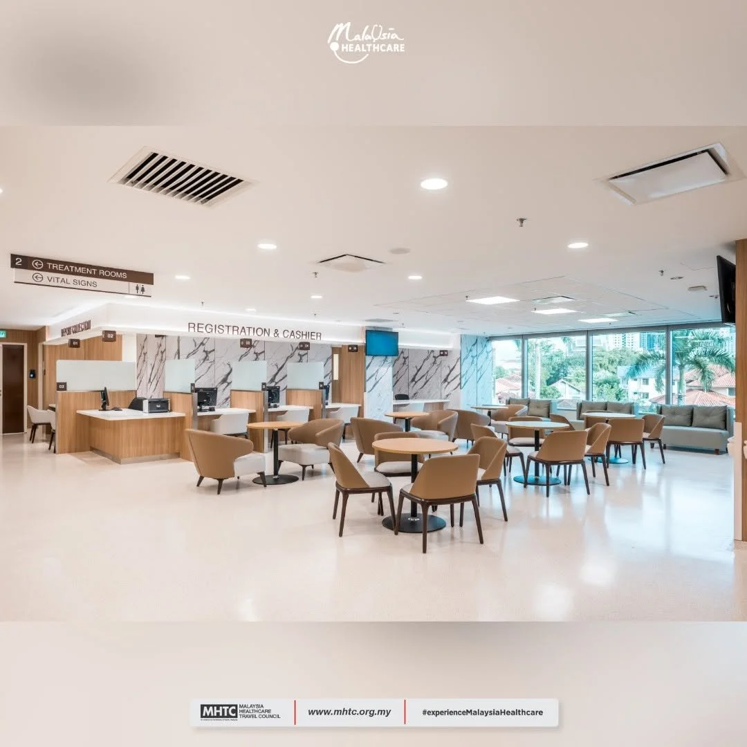 A spacious hospital waiting area with tables and chairs, a registration and cashier desk, and large windows showing outdoor greenery.