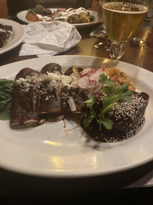 Plate of Mexican food with carne en su jugo topped with cheese, rice with vegetables, and a small amount of shredded lettuce and crab meat, alongside a glass of beer on a restaurant table.