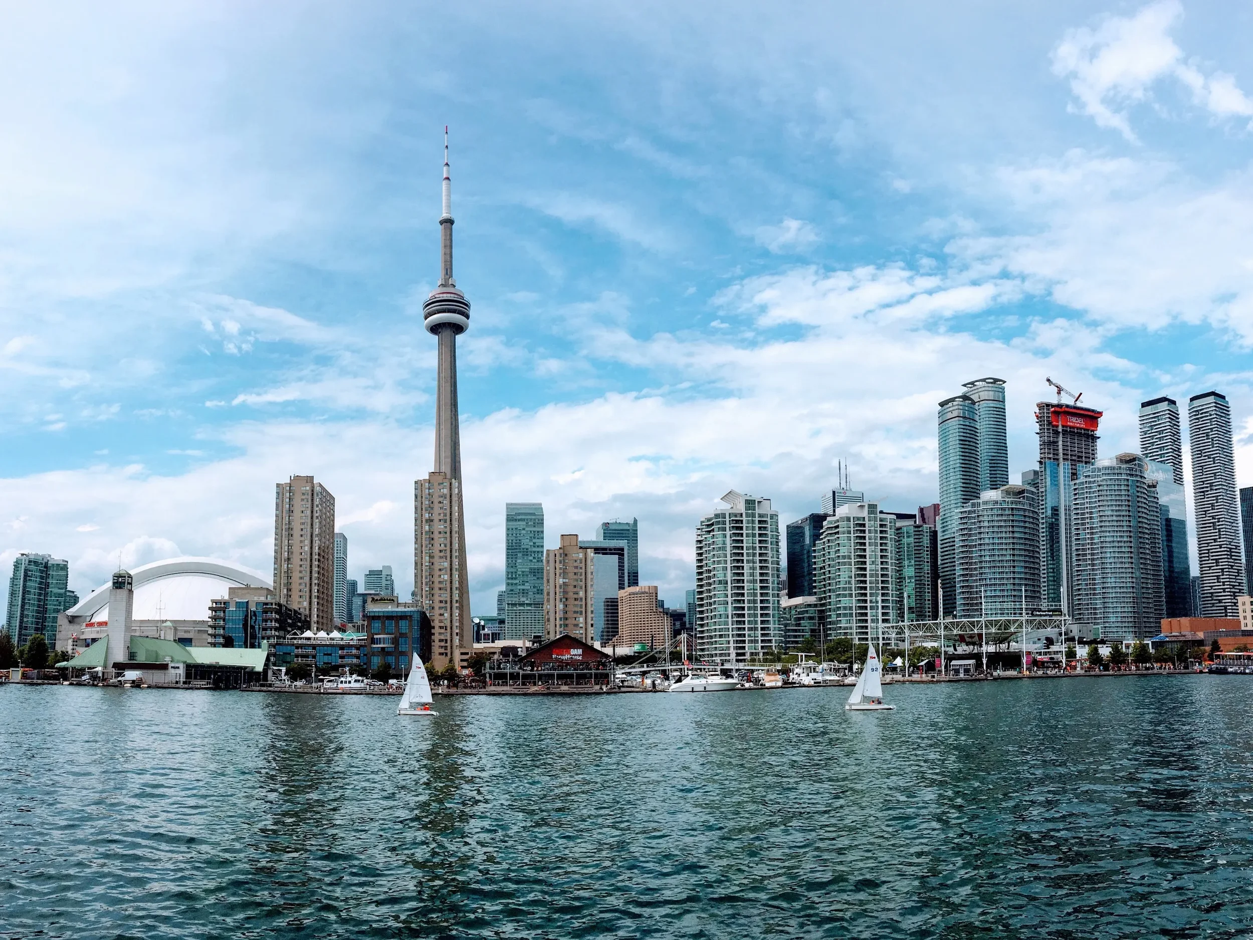 Toronto skyline with CN Tower, high-rise buildings, and sailboats on the water.