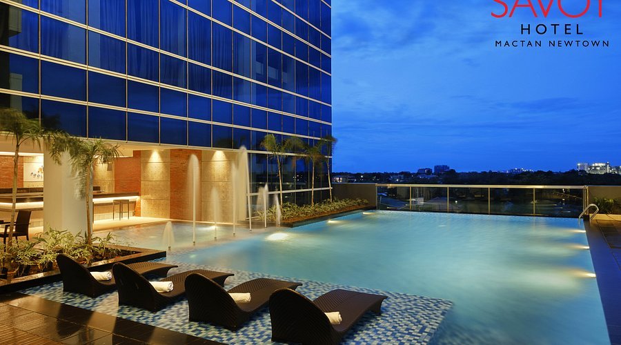 Rooftop swimming pool at sunset with lounge chairs, water features, and city skyline in the background at the Savoy Hotel, Mactan Newtown.