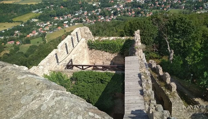 View from atop a historic stone castle overlooking a valley with trees, fields, and houses.
