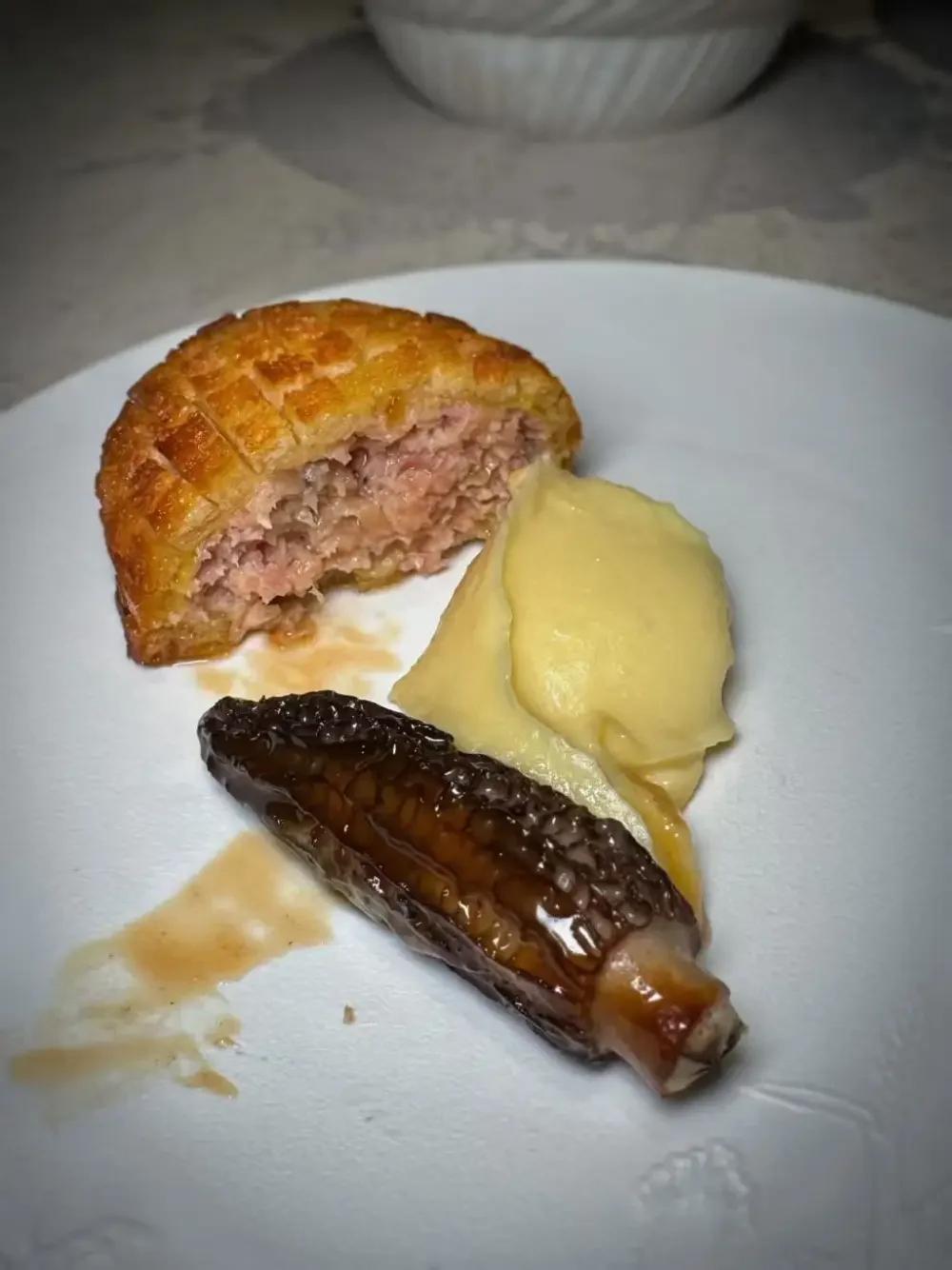 Baked meatloaf stuffed with ham, served with mashed potatoes, glazed eggplant, and gravy on a white plate.