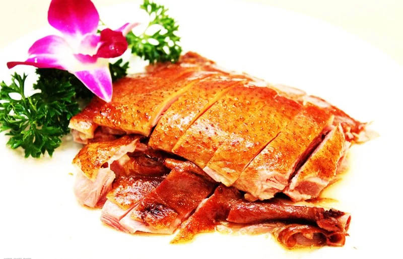 Cooked and sliced roasted duck garnished with parsley and a purple orchid on a white plate