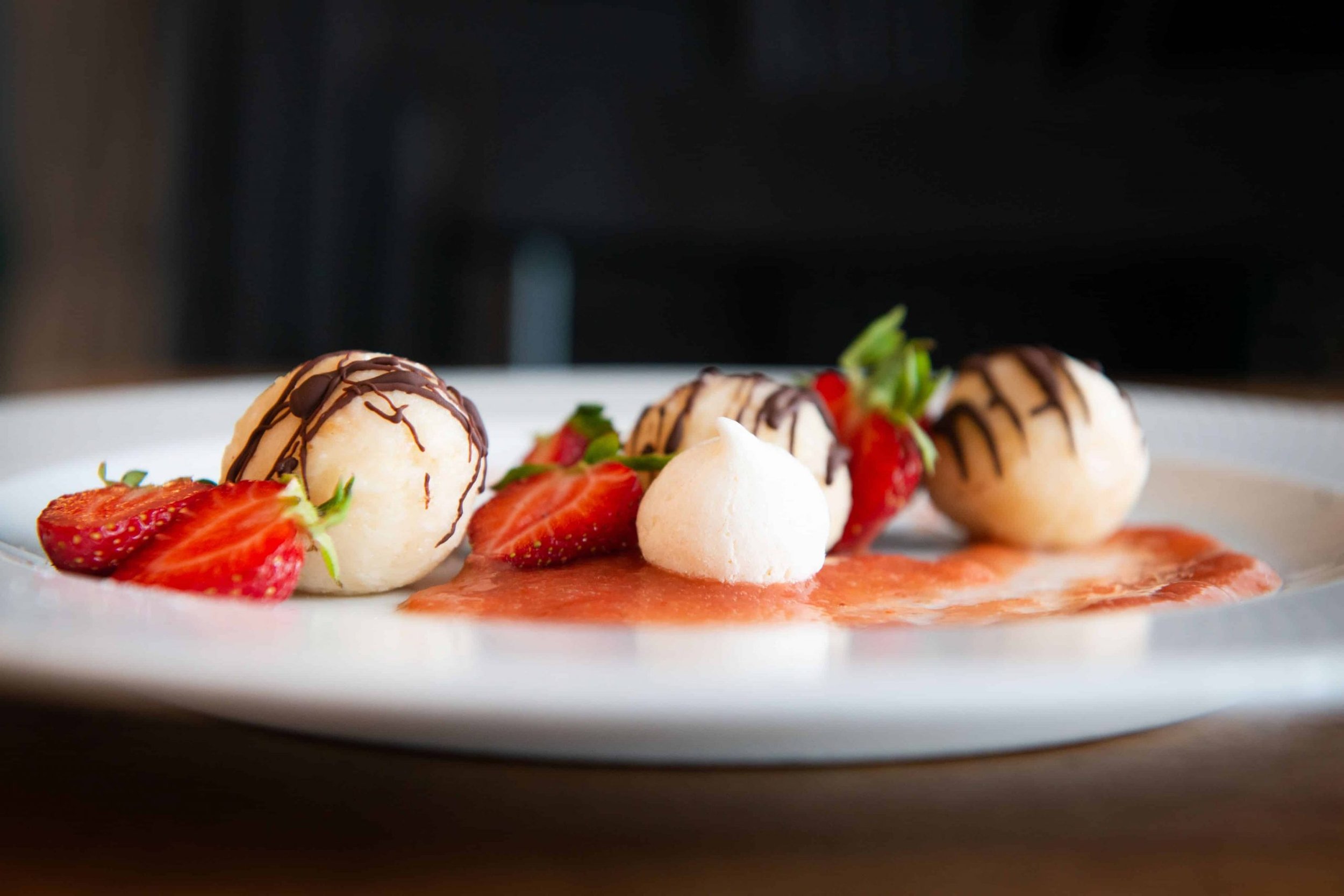 Dessert with strawberries, vanilla ice cream, and white cream ball on a white plate