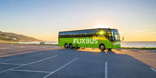 Green FlixBus parked near a body of water at sunset with an empty parking lot in the foreground.