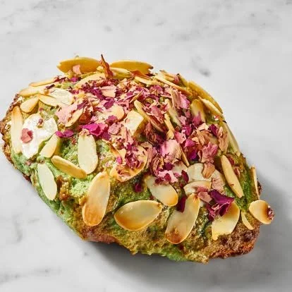 A piece of cake topped with slivered almonds, pink rose petals, and sliced pistachios.
