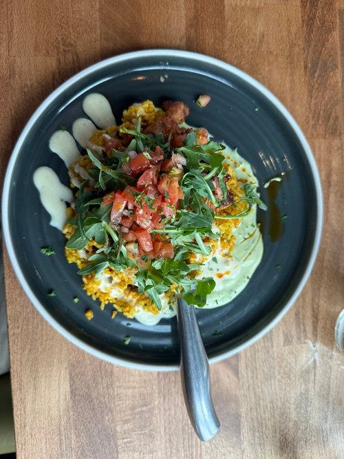 A plate of scrambled eggs topped with chopped tomatoes, arugula, and a drizzle of white and dark sauces